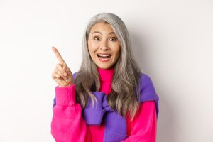 Close up of beautiful asian female model pointing finger at upper left corner, smiling and looking happy at camera, showing promo d